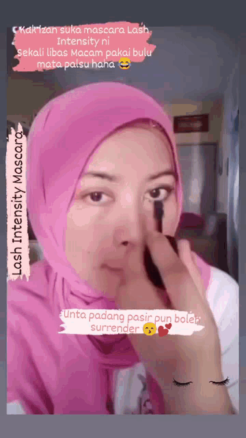 a woman in a pink hijab is applying mascara to her eyelashes