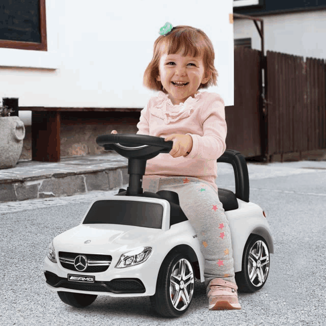 a little girl is riding a white mercedes amg push car