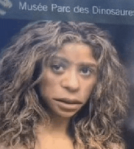 a woman with curly hair is standing in front of a sign .