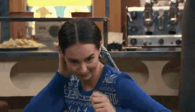 a woman in a blue sweater is sitting at a table in front of a counter in a restaurant .