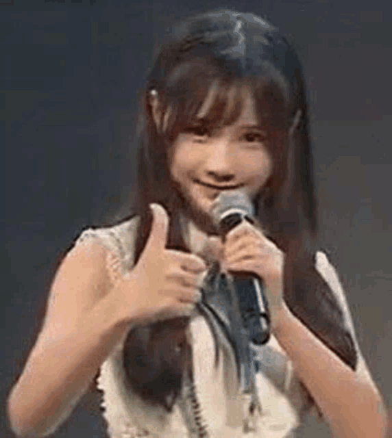 a girl is holding a microphone in her hand and giving a thumbs up .