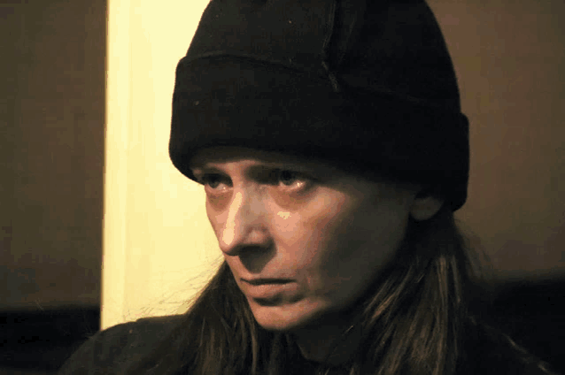 a woman wearing a black beanie looks at the camera with a serious look on her face