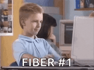 a young boy is sitting at a desk in front of a computer with the words fiber # 1 written on the screen .