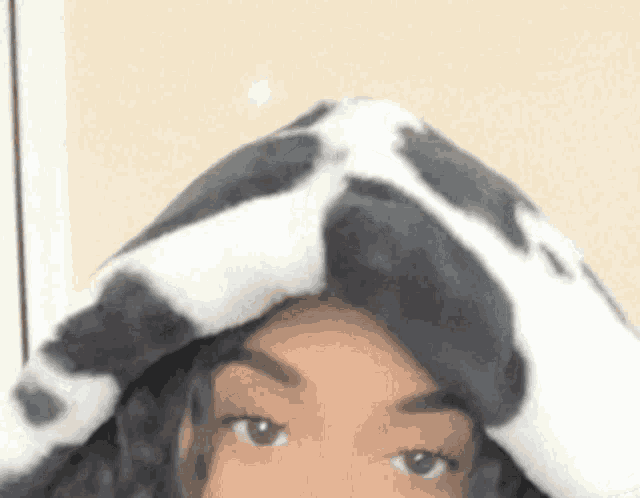 a woman wearing a cow print hat is covering her head with a blanket .