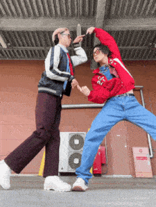 two people are dancing in front of a building and one of them has a jacket that says ' nc state ' on it