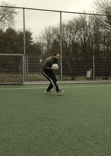 a man holding a soccer ball on a field with trees in the background