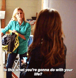 a woman in a blue shirt is holding a laundry basket and talking to another woman in a laundry room