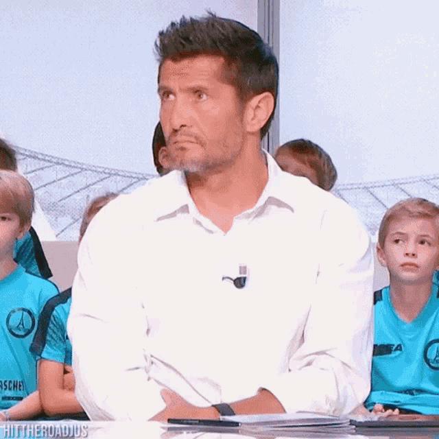 a man in a white shirt is sitting in front of a group of children wearing blue shirts with the word aachen on them