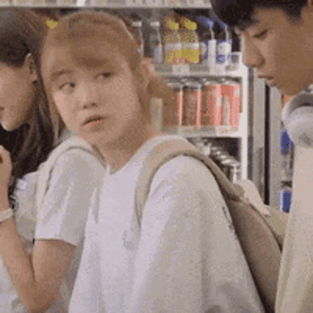 a man and two women are standing next to each other in front of a refrigerator filled with soda .