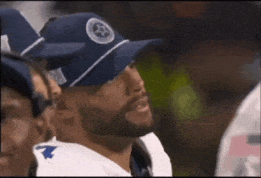 a football player wearing a blue hat with a star on it is sitting in a huddle with his teammates .