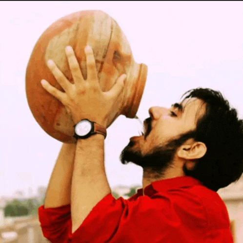 a man in a red shirt is drinking from a pot