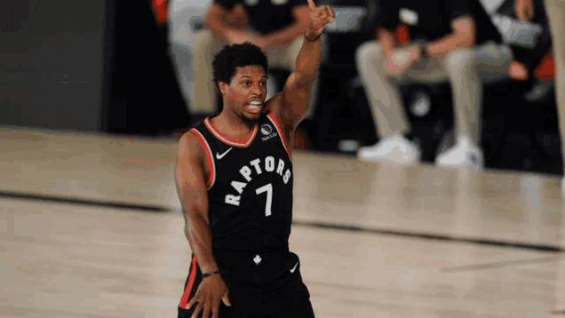 a man wearing a raptors jersey is pointing upwards