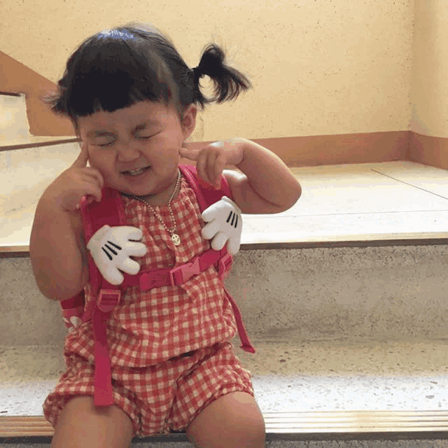 a little girl wearing a mickey mouse glove is sitting on a set of stairs with her eyes closed