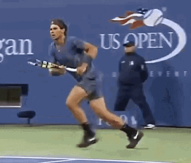 a man is running on a tennis court holding a tennis racquet in front of a us open sign .