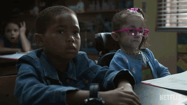 a girl wearing pink glasses sits next to a boy in a classroom with a netflix logo in the background