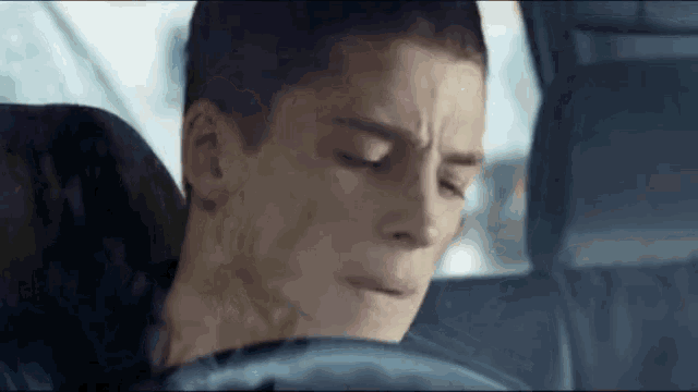 a man is sitting in the driver 's seat of a car with his eyes closed and his mouth open .