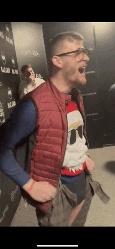 a man wearing a red vest and a christmas sweater is standing in front of a bacardi wall