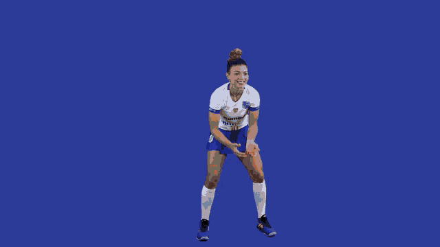 a female volleyball player in a white shirt and blue shorts with a blue background is about to serve the ball