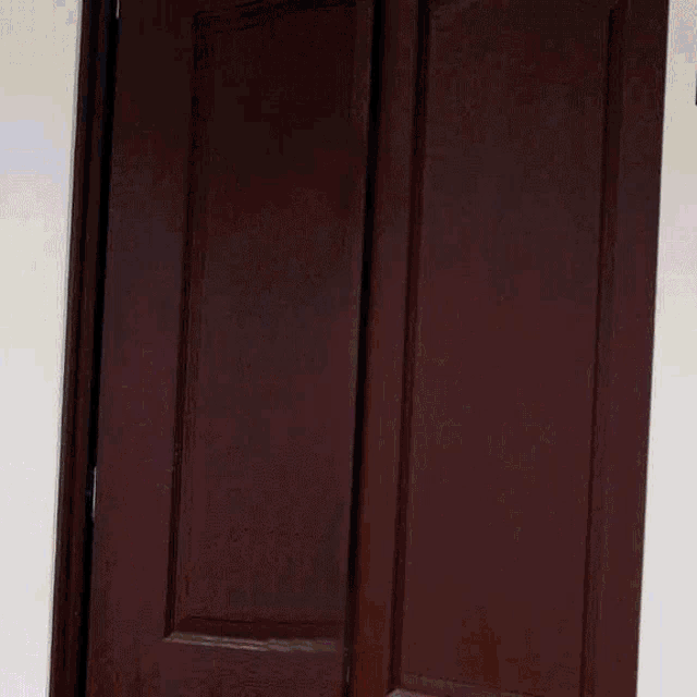 a man in a white shirt and red tie smiles while peeking out from behind a door