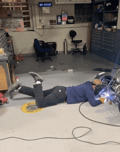 a man laying on the floor in a garage with a yellow sign that says " watch your step "