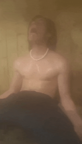 a shirtless man is sitting in a sauna with his eyes closed and his mouth open .