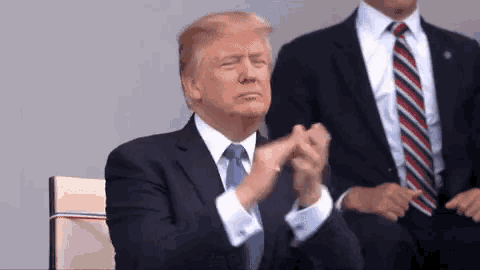 donald trump is clapping his hands while sitting in a chair