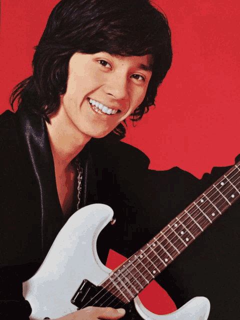 a young man is holding a white guitar and smiling for the camera