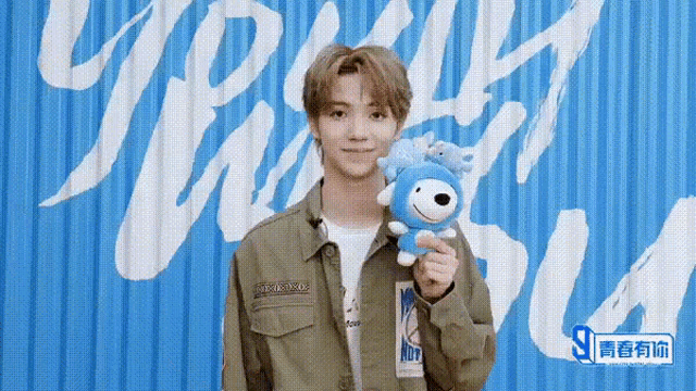 a young man is holding a stuffed animal in front of a blue wall with the word youth on it .