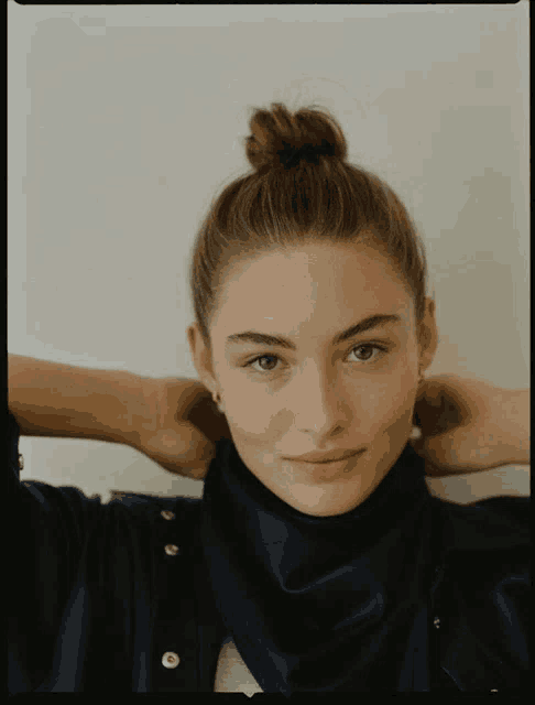 a woman with her hair in a bun has her hands behind her head