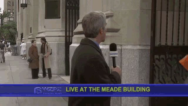 a man is holding a microphone in front of a sign that says ' live at the meade building '