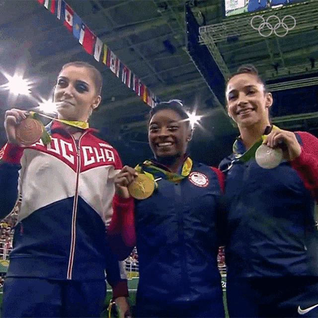 three female gymnasts are posing for a picture with one wearing a jacket that says ' dc chg ' on it