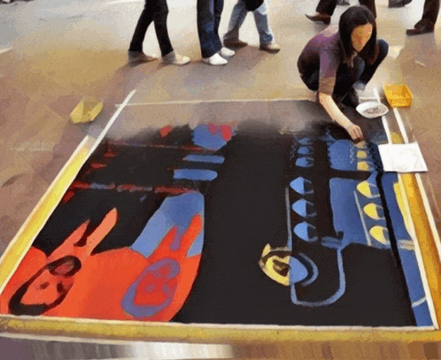 a woman is kneeling on the floor painting a colorful picture