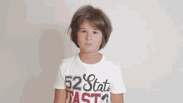 a young boy wearing a white t-shirt with the words `` 52 state fast '' on it is making a funny face .