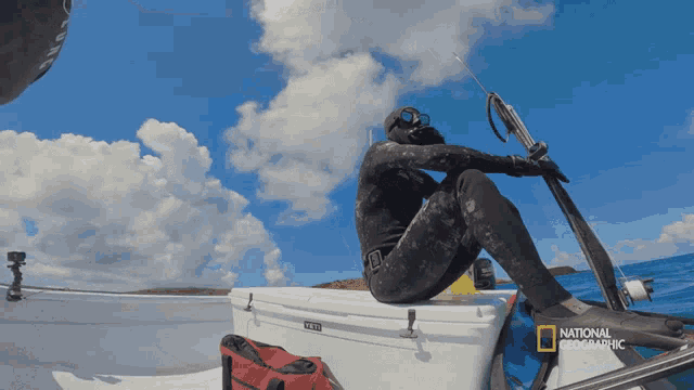 a man in a wet suit sits on the back of a boat that says national geographic on the bottom