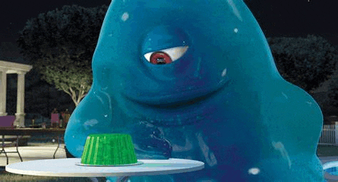 a blue monster is sitting at a table with a green jelly cup .