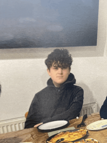 a young boy sits at a table with plates of food on it