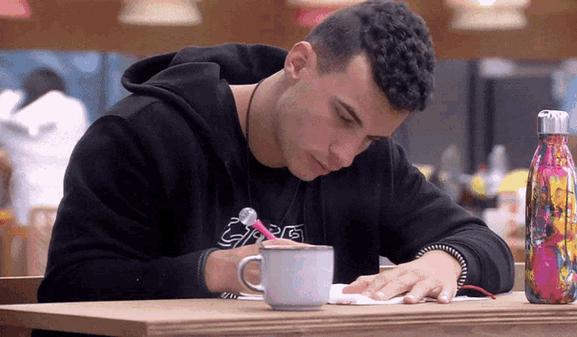 a man is sitting at a table with a cup of coffee and a water bottle with a rainbow design on it