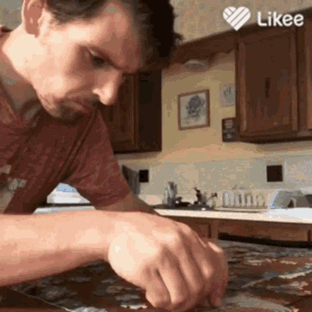 a man in a red shirt is sitting at a table in a kitchen with a likee heart above him