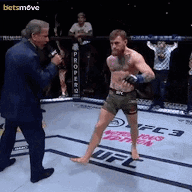 a man in a suit is talking into a microphone while a fighter stands in front of a ufc sign