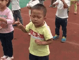 a group of children are dancing on a track . one of the children is wearing a yellow shirt with chinese characters on it .