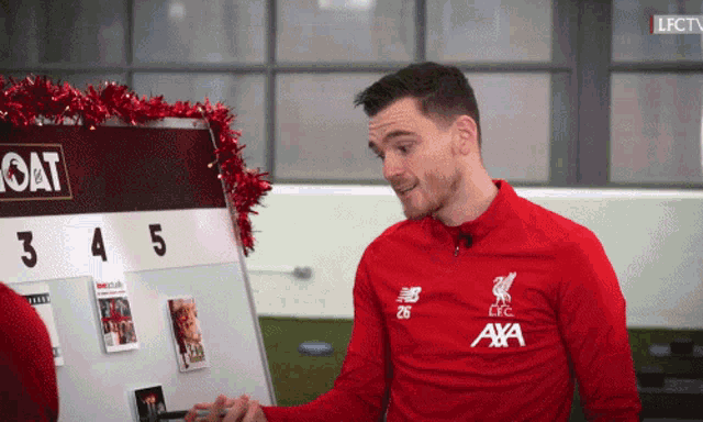 a man in a red lfc shirt stands in front of a board with the number 3 and 5 on it