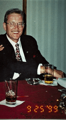 a man in a suit and tie sits at a table with glasses of beer