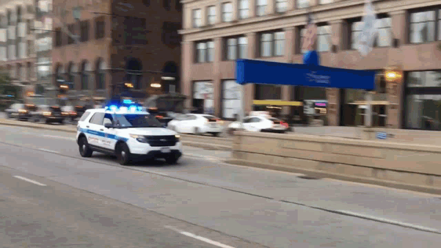 a police car is driving down a street in front of a building with a blue sign that says post office