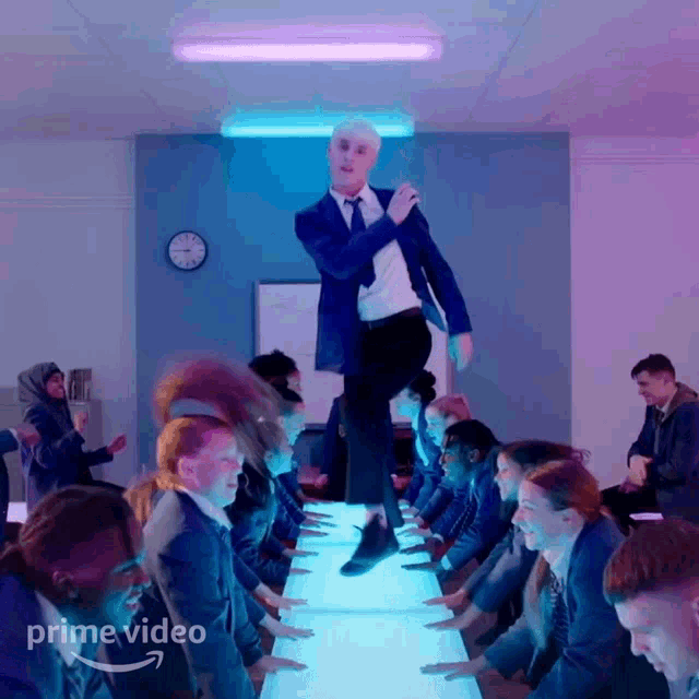 a man in a suit and tie is jumping over a row of people in a room with the words prime video on the bottom right