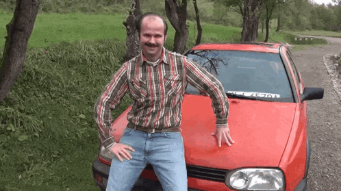 a man standing in front of a red car with a sticker on the windshield that says ' a / a '