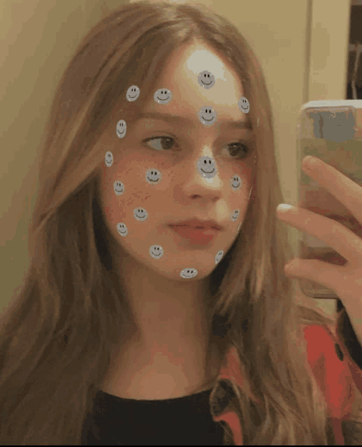 a girl with smiley faces on her face is taking a selfie