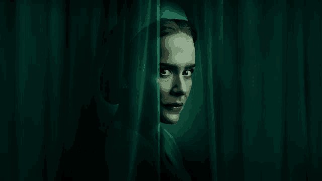 a woman peeking out from behind a green curtain with her eyes closed