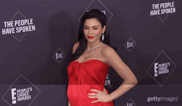 a woman in a red dress is standing in front of a wall that says " the people have spoken "