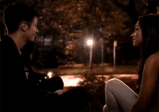 a man and a woman are sitting next to each other in a dark park at night .