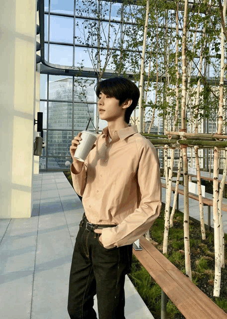 a young man holding a cup of coffee in front of a building